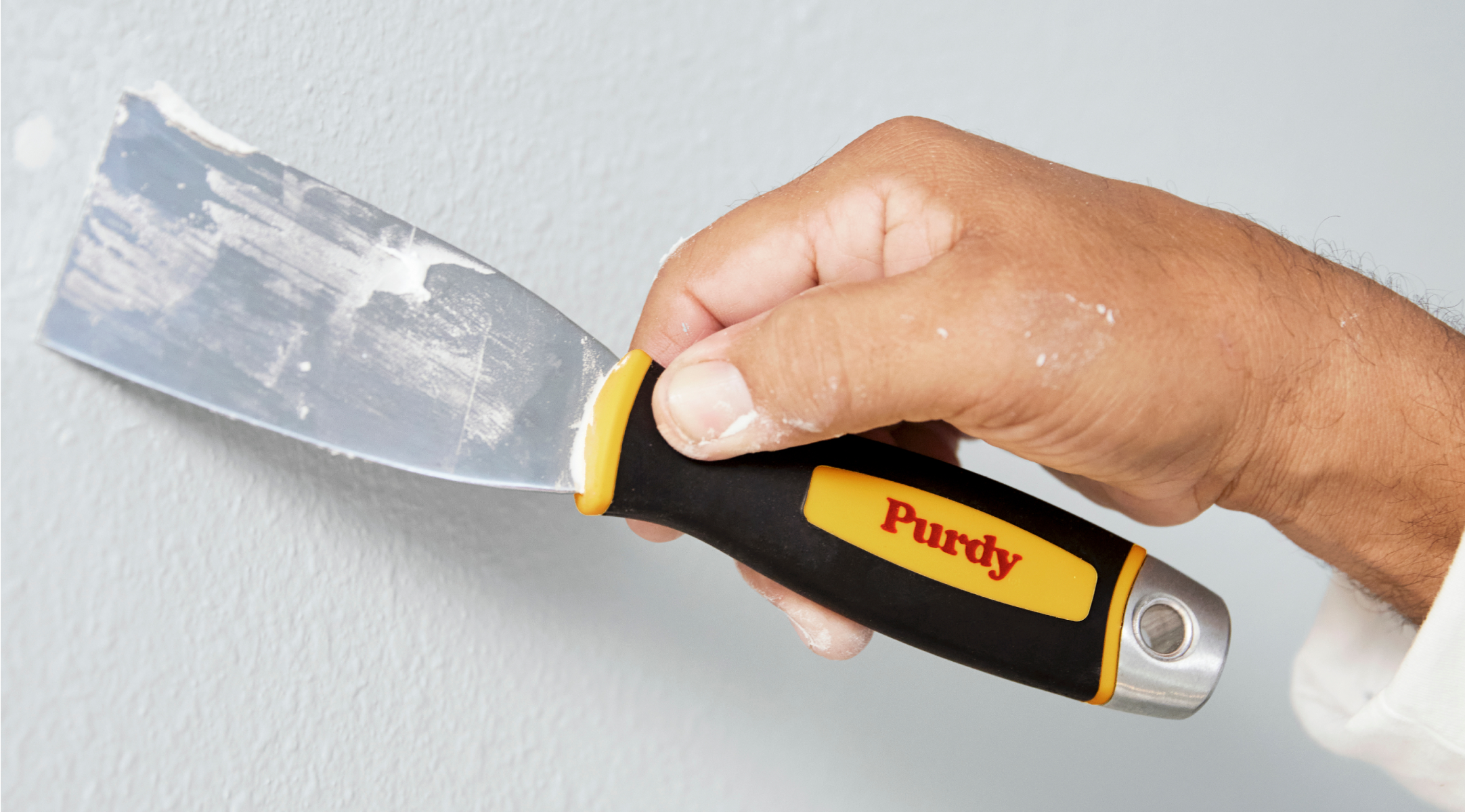 Painter filling holes in the wall with a Purdy putty knife.